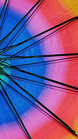 Close-up view of a colorful umbrella's spokes against a bright rainbow fabric. Abstract pattern with radiating lines.の写真素材