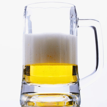 A close-up shot of a glass beer mug filled with golden beer and a thick layer of white foam on top.の写真素材