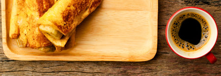 Crispy golden French toast sticks served on a wooden board next to a steaming cup of black coffee.の写真素材