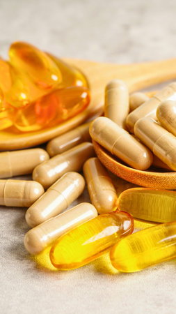 A collection of softgel capsules, some appearing to be fish oil, are artfully arranged on a textured wooden surface.の写真素材