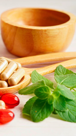 A wooden bowl, spoon with capsules, fresh greens, and red berries suggest natural health and wellness.の写真素材