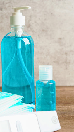 A large pump bottle and a smaller bottle of blue liquid soap sit on a white cloth with a textured wall behind them.の写真素材