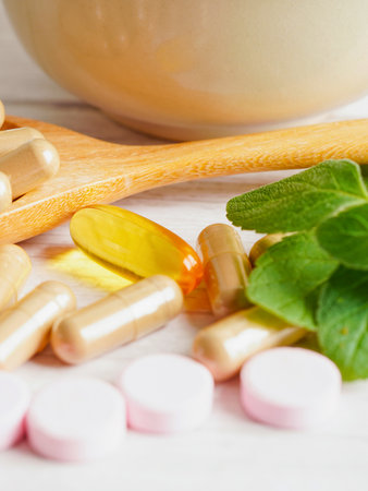 A close-up shot of various pills, capsules, and fresh green herbs arranged with a wooden spoon and a bowl.の写真素材