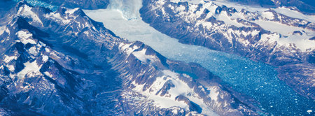 An aerial view of rugged, snow-capped mountains with a winding glacial river flowing through the valley below.の写真素材