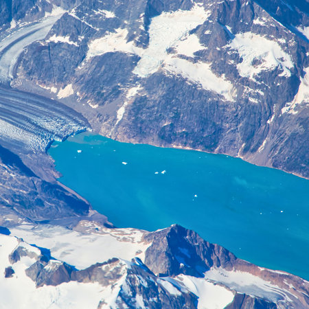 An aerial view showcases a vibrant turquoise lake nestled within rugged, snow-dusted mountain peaks, creating a stunning natural landscape.の写真素材