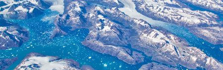 An abstract, high-angle view of rugged, snow-dusted mountains meeting vibrant turquoise water with scattered white specks.の写真素材