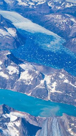 An aerial view of a vast arctic landscape featuring a winding turquoise river or lake surrounded by snow-covered terrain and ice.の写真素材