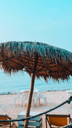 A thatched umbrella stands on a sandy beach, offering shade with the ocean and sky in the background.の写真素材
