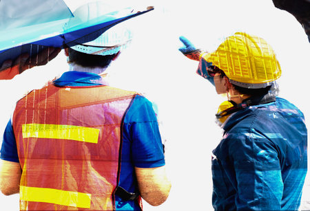 Two construction workers wearing hard hats and safety vests are seen from behind, one pointing to something out of frame.の写真素材