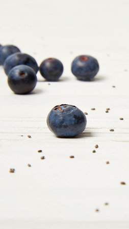 A close-up shot of several ripe blueberries scattered across a light-colored surface, with a few tiny seeds visible.の写真素材