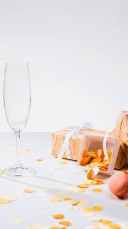 An empty wine glass sits on a table scattered with confetti, next to a partially opened gift box, suggesting a recent celebration.の写真素材