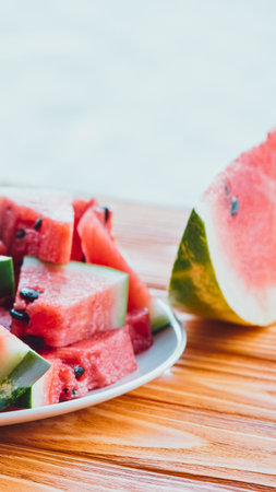 Juicy, refreshing watermelon slices arranged on a white plate next to a large wedge on a wooden surface.の写真素材