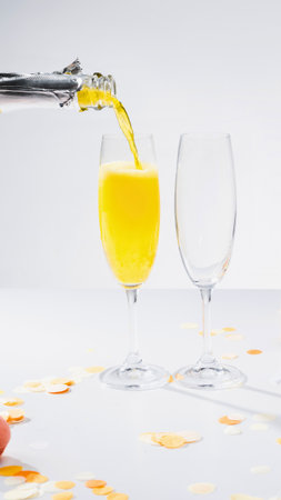 A stream of bright yellow liquid is poured from a metallic nozzle into a clear glass, with another empty glass beside it.の写真素材