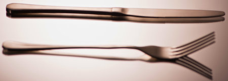A knife and fork are positioned on a light surface, creating distinct shadows and reflections, suggesting a clean and minimalist aesthetic.の写真素材