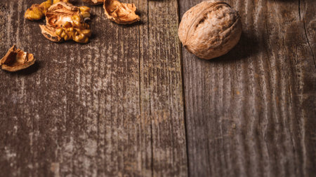 A close-up shot of whole and broken walnuts scattered on a textured, dark wooden background with warm lighting.の写真素材