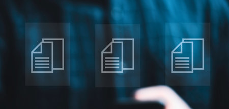 Three stylized document icons are displayed on a dark, blurred blue background, suggesting digital information or data management. A finger is visible, interacting with the interface.の写真素材