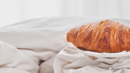 A close-up of a freshly baked, golden brown croissant nestled on soft, white fabric, creating a simple and elegant still life.の写真素材