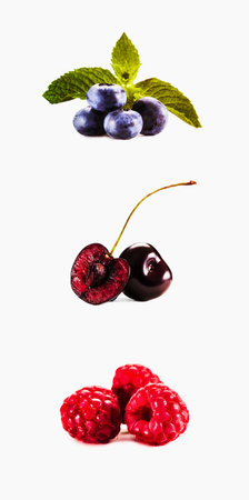 A vertical arrangement of blueberries with mint, cherries, and raspberries presented against a clean...