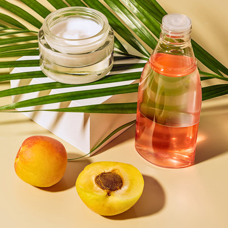 A jar of cream, a bottle of serum, and fresh apricots are arranged with palm leaves, suggesting natural beauty products.の写真素材