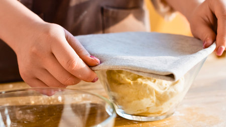 Close up of hands stretching a flexible silicone lid over a glass bowl filled with food, preparing...