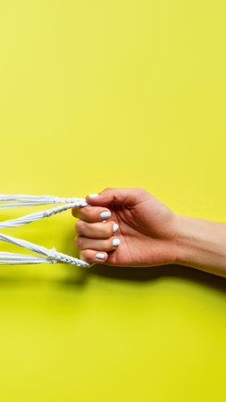 A woman's hand with long, manicured white nails is holding several white strings against a vibrant yellow backdrop.の写真素材