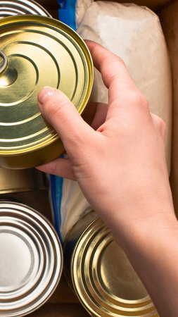 A close-up shot of a hand selecting a can from a collection of food items, likely for donation or storage.の写真素材