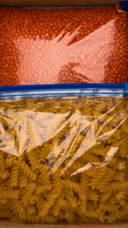 Two clear plastic bags filled with dry pasta and red lentils, stacked vertically, ready for pantry storage.の写真素材