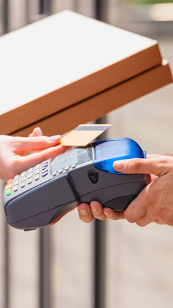 A person uses their smartphone to make a contactless payment at a point of sale terminal on an outdoor table.の写真素材