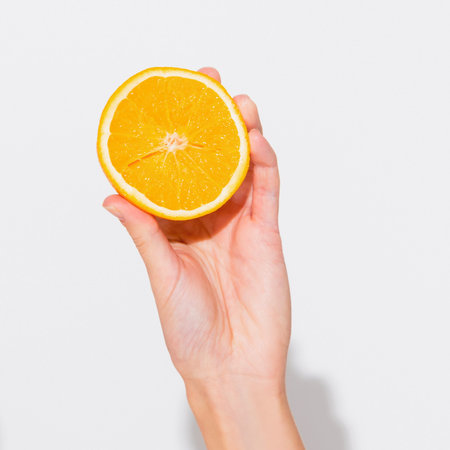 A person's hand gently holds a vibrant, juicy orange slice. The bright citrus fruit is presented against a clean white backdrop.の写真素材