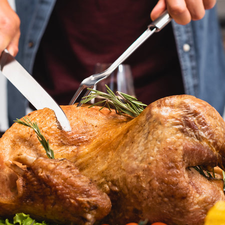 A close-up shot of hands carving a golden-brown roasted turkey, garnished with fresh rosemary, ready for a festive meal.の写真素材