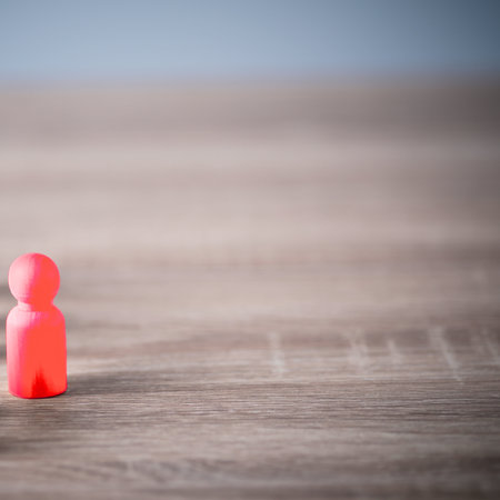 A single, small, bright red figure stands in sharp focus on a blurred wooden background, emphasizing its isolation.の写真素材