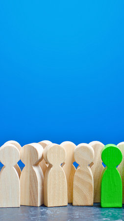 A single green wooden figure stands out from a group of similar wooden figures against a bright blue background.の写真素材