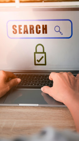 Close-up of hands typing on a laptop keyboard. A search bar with a lock icon indicates secure online activity.の写真素材