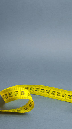 A bright yellow measuring tape is loosely coiled on a smooth, gray background, showcasing its markings and flexibility.の写真素材