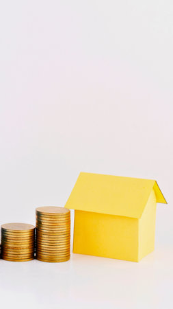 Three stacks of gold coins increase in height, leading towards a bright yellow house, representing financial progress and homeownership.の写真素材