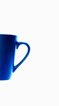 A close-up shot of a deep blue ceramic mug with a curved handle, isolated on a stark white background.の写真素材