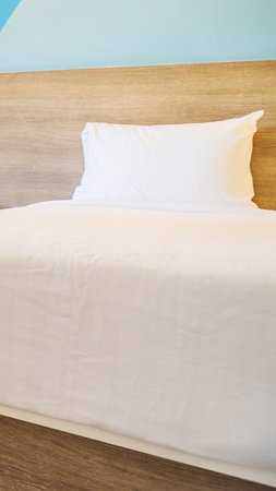A close-up view of a neatly made bed featuring a white pillow and light-colored bedding, with a...