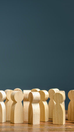 A collection of light-colored wooden peg people stand together on a wooden surface against a dark blue background.の写真素材