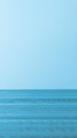 A serene, minimalist depiction of the ocean meeting the sky at the horizon. The water is a deep blue with subtle wave patterns.の写真素材