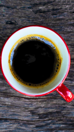 A top-down view of a steaming cup of dark black coffee with a rich crema, resting on a rustic wooden table.の写真素材