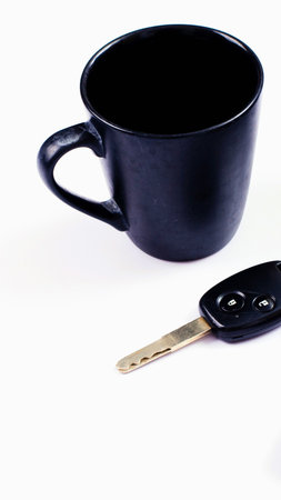 A black coffee cup sits next to a car key on a clean white surface, suggesting morning routine or travel preparation.の写真素材
