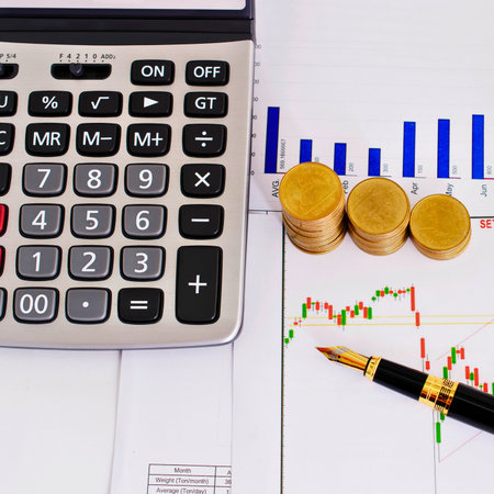 A close-up shot shows a calculator, stacks of coins, and financial charts, suggesting financial planning and analysis.の写真素材