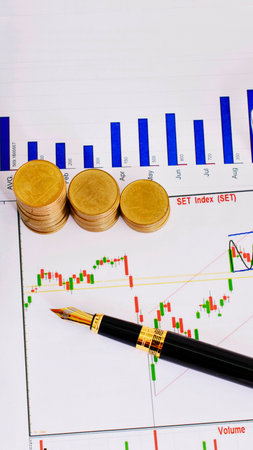 A financial chart displays market trends with three gold coins and a pen, symbolizing investment and analysis.の写真素材