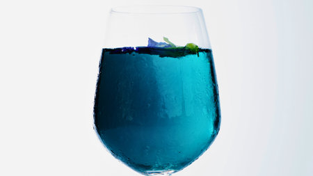 A close-up of a tall wine glass filled with a bright blue liquid and a small garnish on top, against a white background.の写真素材