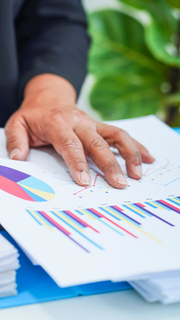 A close-up shot of an elderly person's hand resting on a stack of financial documents and charts, suggesting analysis or review.の写真素材