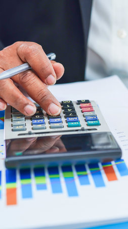 A person's hand is shown operating a calculator over a colorful financial graph, indicating financial analysis and calculation.の写真素材