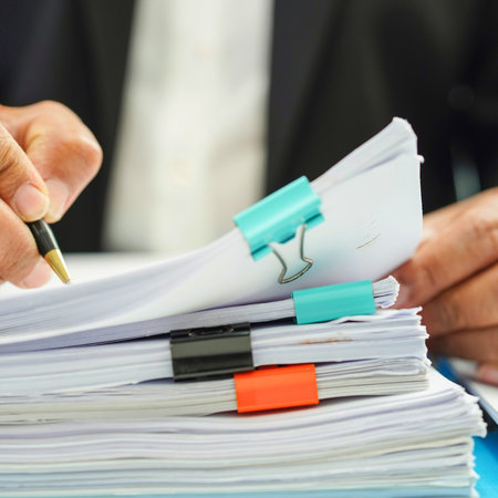 A close-up shot shows a person's hands holding a pen and reviewing a stack of papers secured with colorful clips.の写真素材