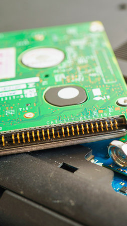 A detailed view of a computer hard drive's green circuit board with its metallic pins visible, resting on a dark, textured surface.の写真素材
