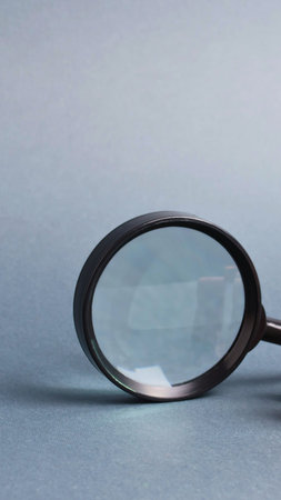 A close-up of a magnifying glass with a dark frame resting on a textured, muted blue surface.