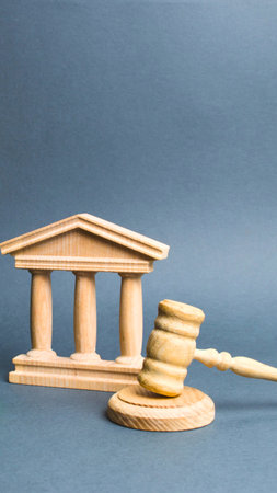 A wooden gavel rests beside a miniature wooden courthouse with pillars, representing legal proceedings and the justice system.の写真素材